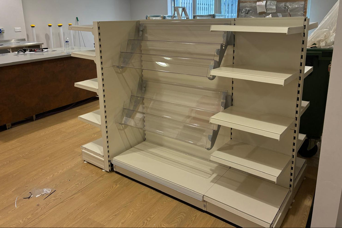 An empty retail shelving unit in cream with magazine shelves within an empty hospital shop