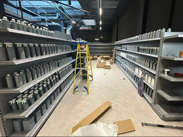 Grey linear retail shop shelving with non-descript products on display during the construction phase. 